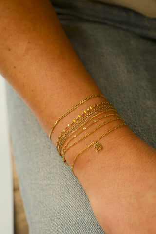 The Bond Society layered gold chain bracelets with charm detail, minimalist fine jewelry styled on woman’s wrist with denim.