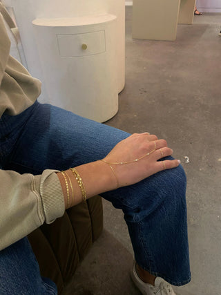 The Bond Society delicate gold chain bracelets styled on woman's wrist with casual jeans and neutral top, minimalist everyday jewelry look.