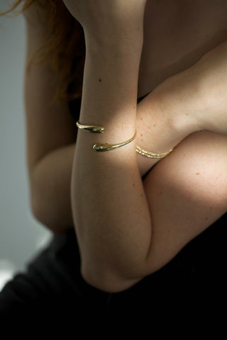 Minimalist gold cuff bracelets on woman's crossed arms, modern jewelry fashion photography with soft natural light.