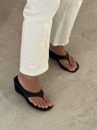 The Bond Society minimalist gold anklet styled with white trousers and black wedge sandals, elegant everyday jewelry accessory.