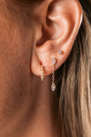 Woman's ear stack featuring a diamond bezel hoop, diamond stud and diamond chain drop earring