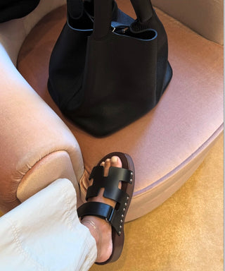 The Bond Society delicate layered gold anklets styled with white trousers and black leather sandals, minimalist fine jewelry look.