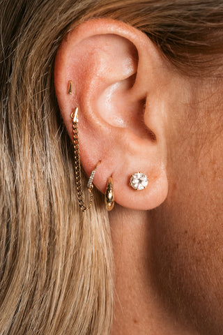Close-up of an ear with gold earrings and a diamond stud earring.