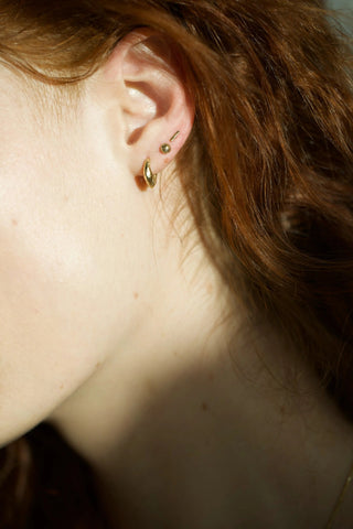 Sleek miniature bar stud earrings in 14k gold, worn on ear
